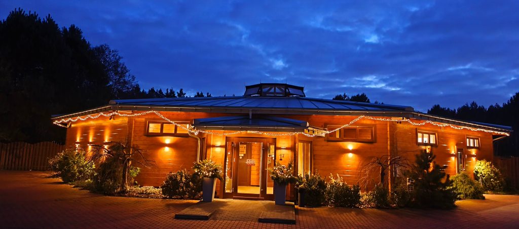 Budynek Sauny Olimpia o zmroku, udekorowany świątecznymi lampkami – widok wejścia podczas okresu Bożego Narodzenia.